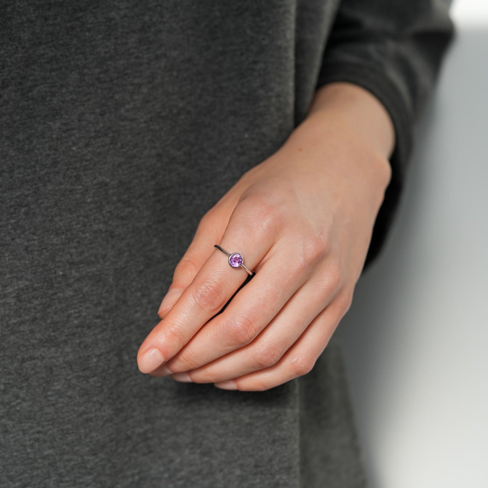 Hand wearing a ring with a purple gemstone against a gray background